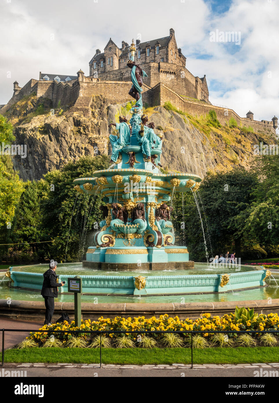 A tourist with a camera admires the refurbished Ross Fountain in West Princes Street Gardens, in front of Edinburgh Castle. Scotland. Stock Photo