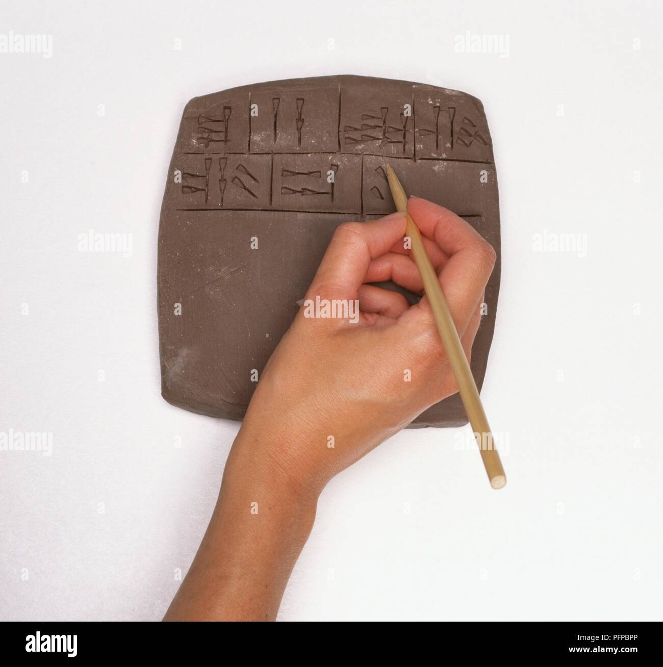 Hand using a pointed reed to write cuneiform script on slab of clay, close-up Stock Photo
