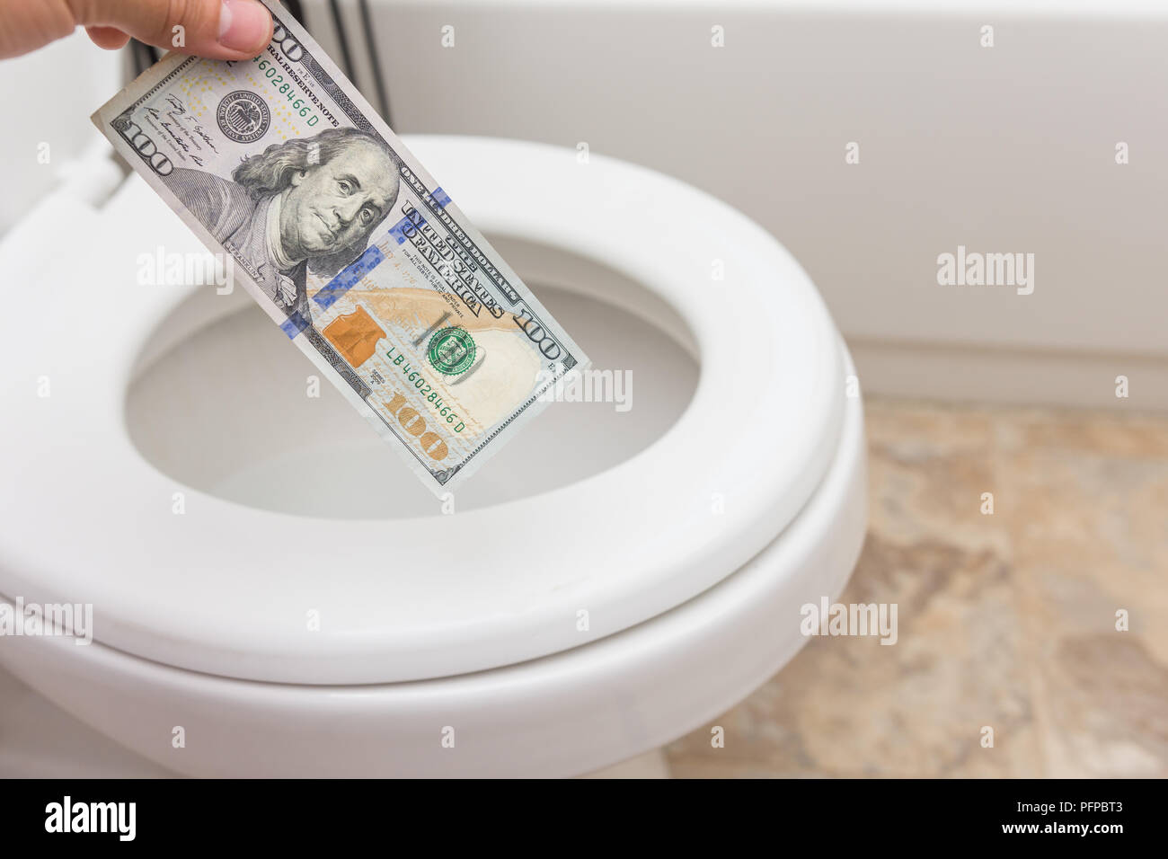 Holding crisp one hundred dollar bill into toilet; clean and bright; finance concept Stock Photo