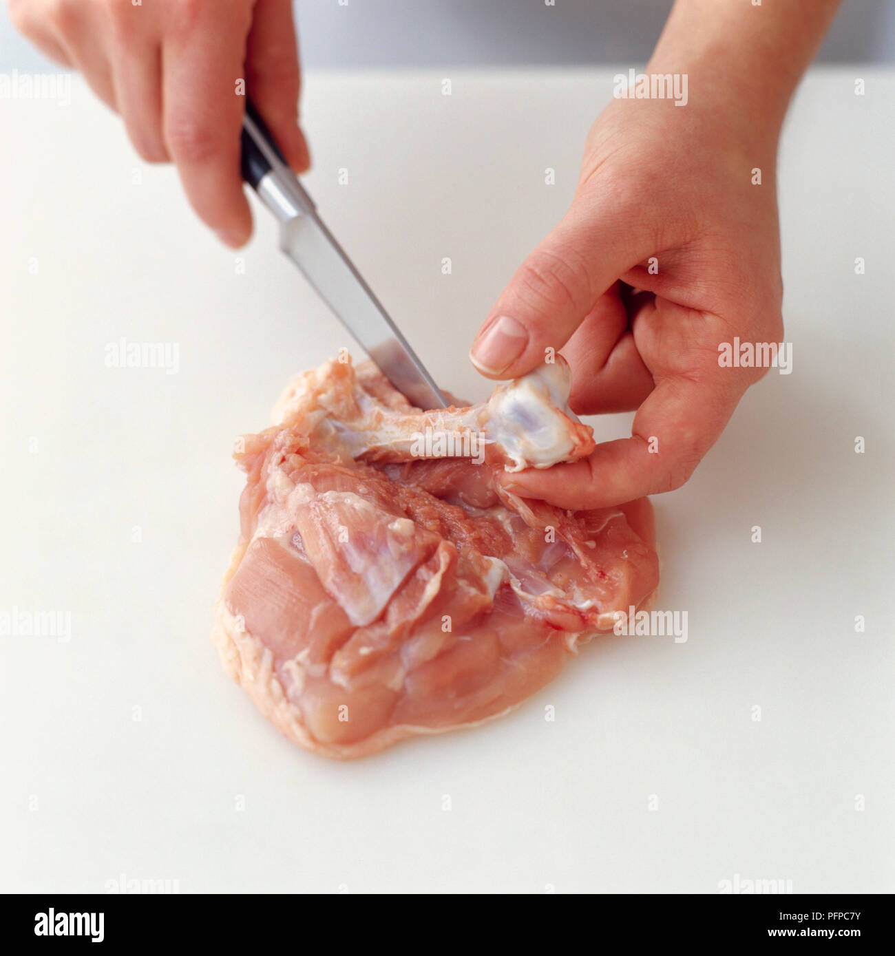Using kitchen knife to remove bone from chicken thigh Stock Photo