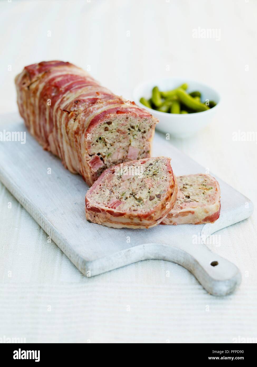 Country terrine sliced on chopping board with bowl of gherkins in