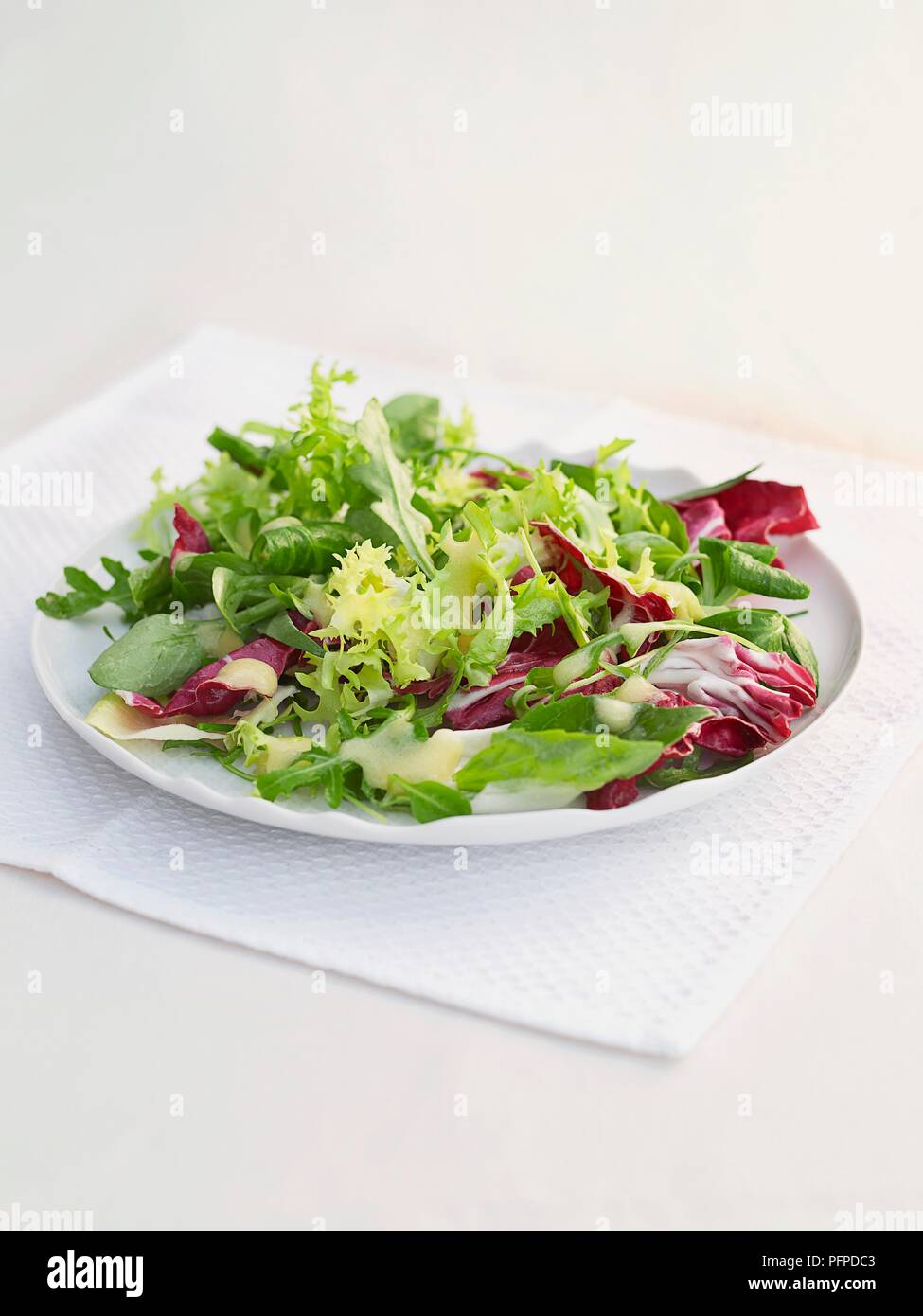 Green and red leaf salad on white plate with napkin on table Stock Photo