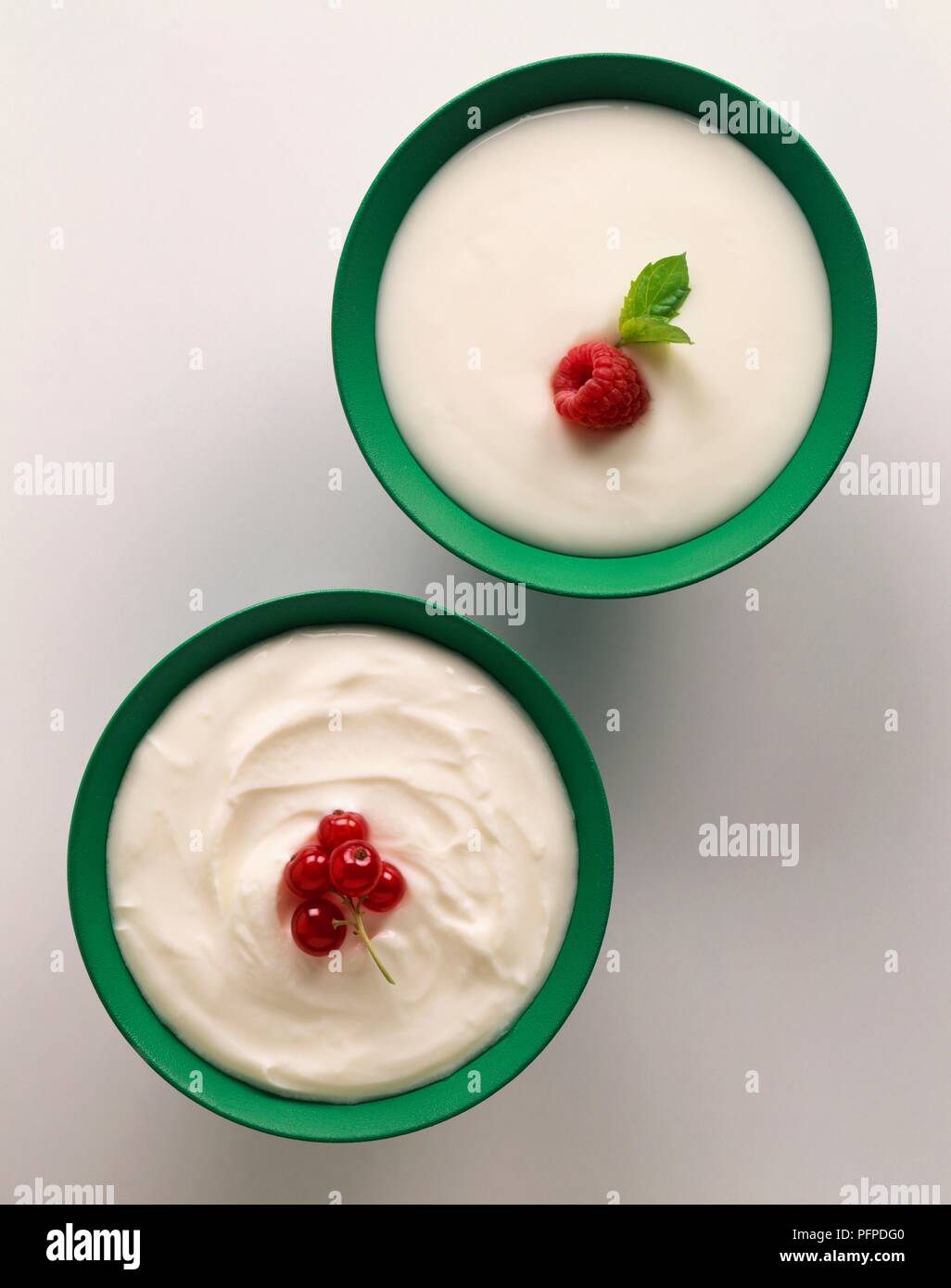Bowls of yoghurt, whole-milk yoghurt garnished with recurrants, and live natural yoghurt garnished with a raspberry Stock Photo
