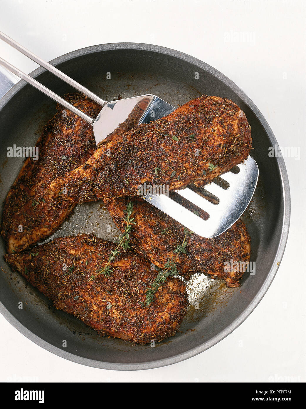 Cajun-style chicken in a pan with one piece on a spatula Stock Photo - Alamy