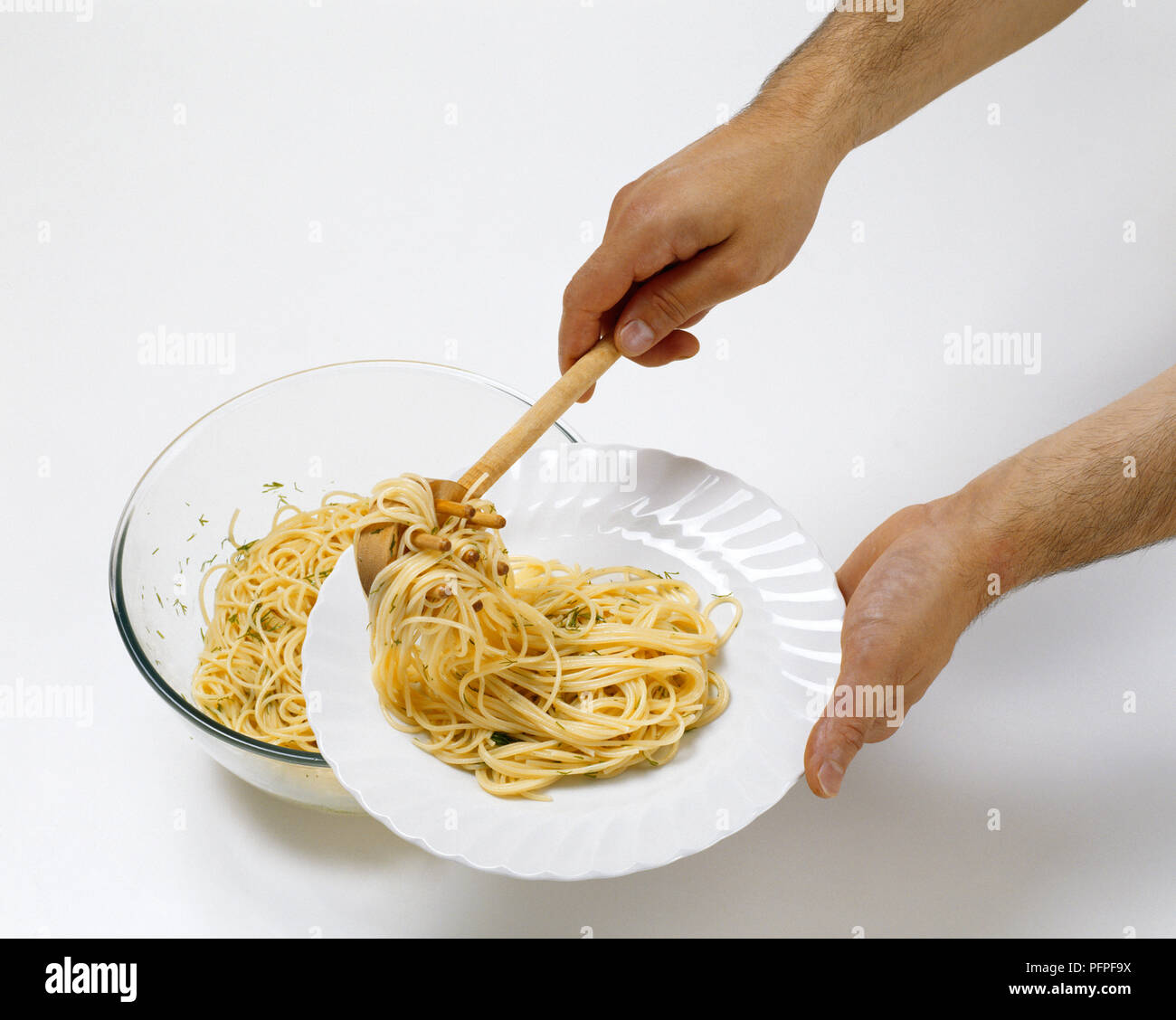 Man using wooden pasta ladle to serve cooked spaghetti on white plate