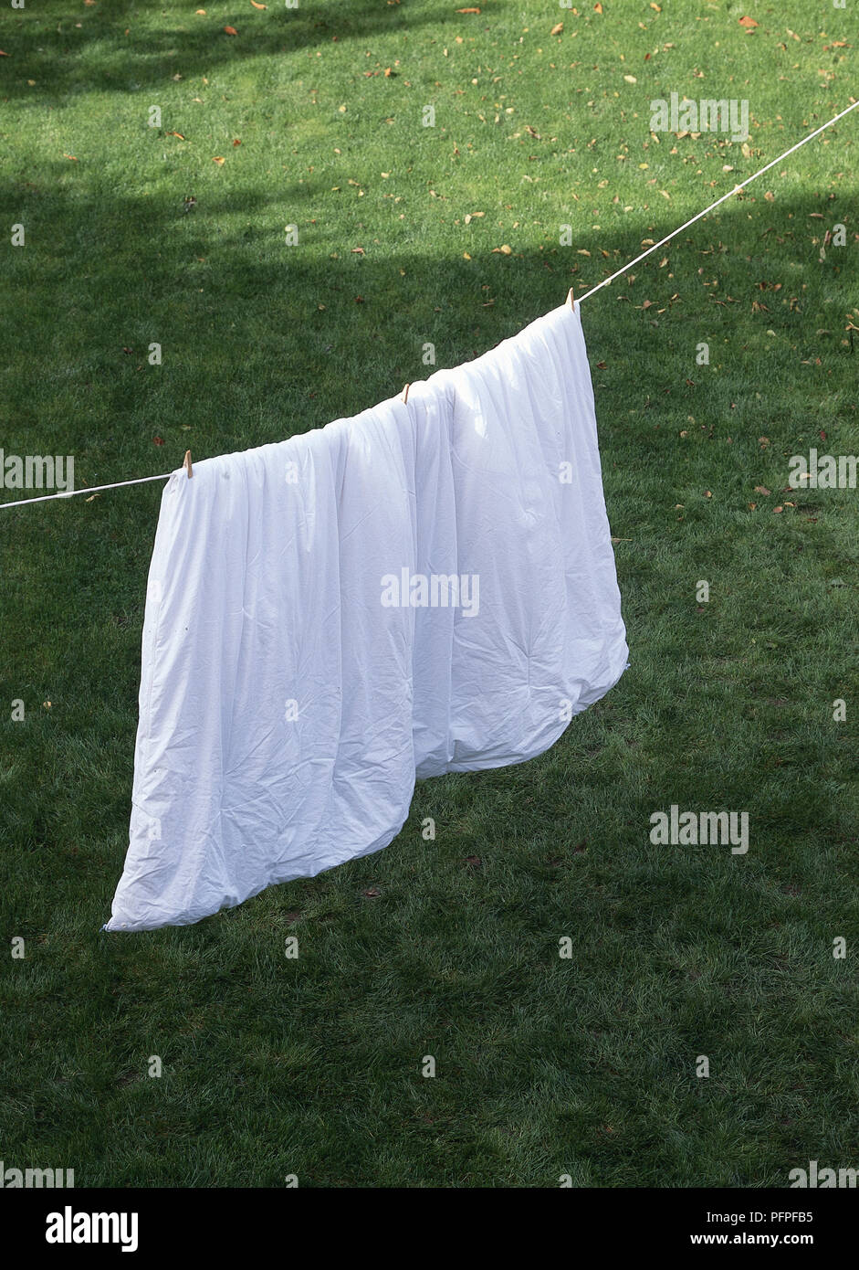 Duvet hanging out to air on washing line above garden lawn. Stock Photo