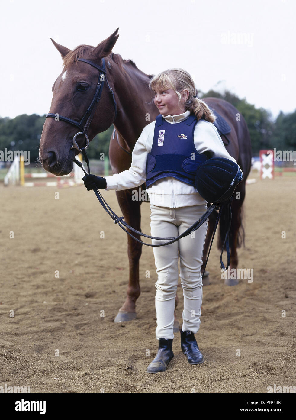 Young girl in paddock wearing riding habit standing next pony, holding  reins, and hat Stock Photo - Alamy