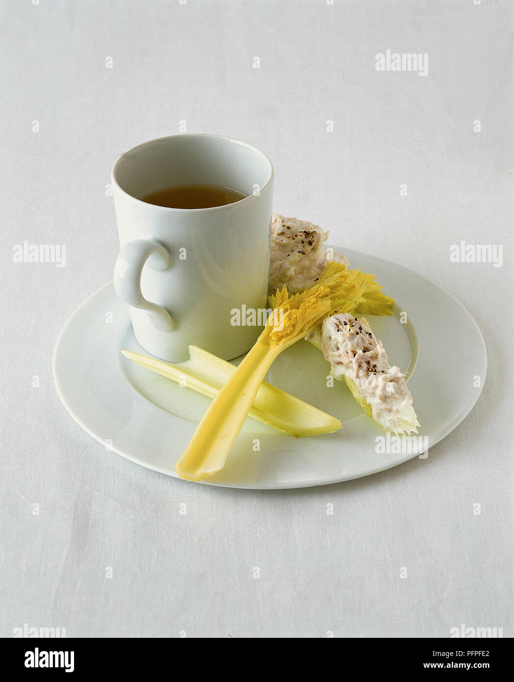 Mug of clear soup served with tuna dip on celery stick Stock Photo
