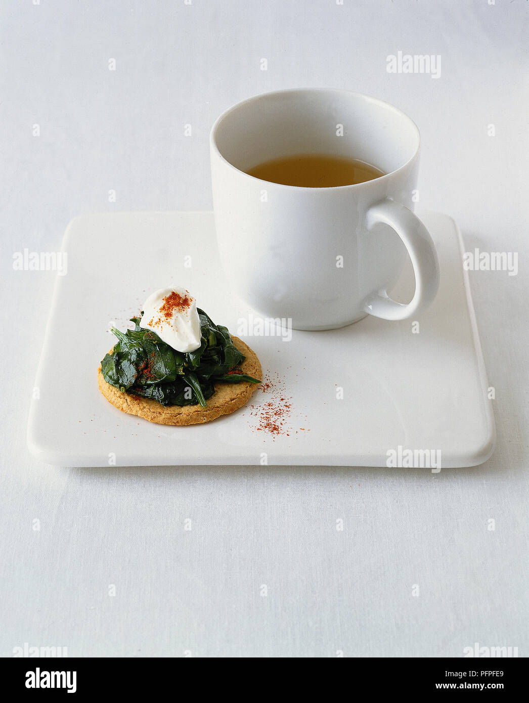 Cup of clear soup served with oatcake, topped with spinach and live natural yoghurt and sprinkled with cayenne pepper Stock Photo