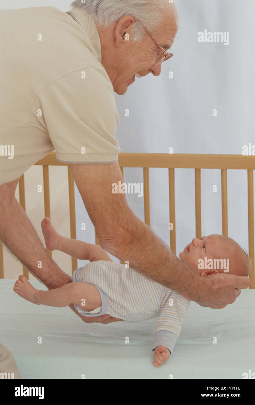 Grandfather putting baby boy in cot, supporting baby's head and rear Stock Photo Alamy