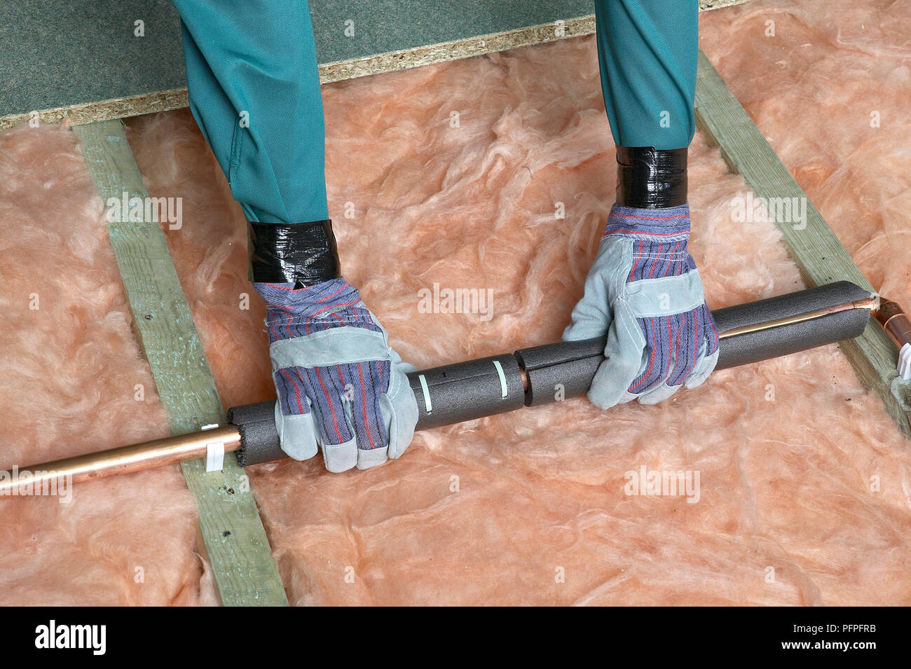 Pipe insulation being put over copper pipe, above joists and insulation
