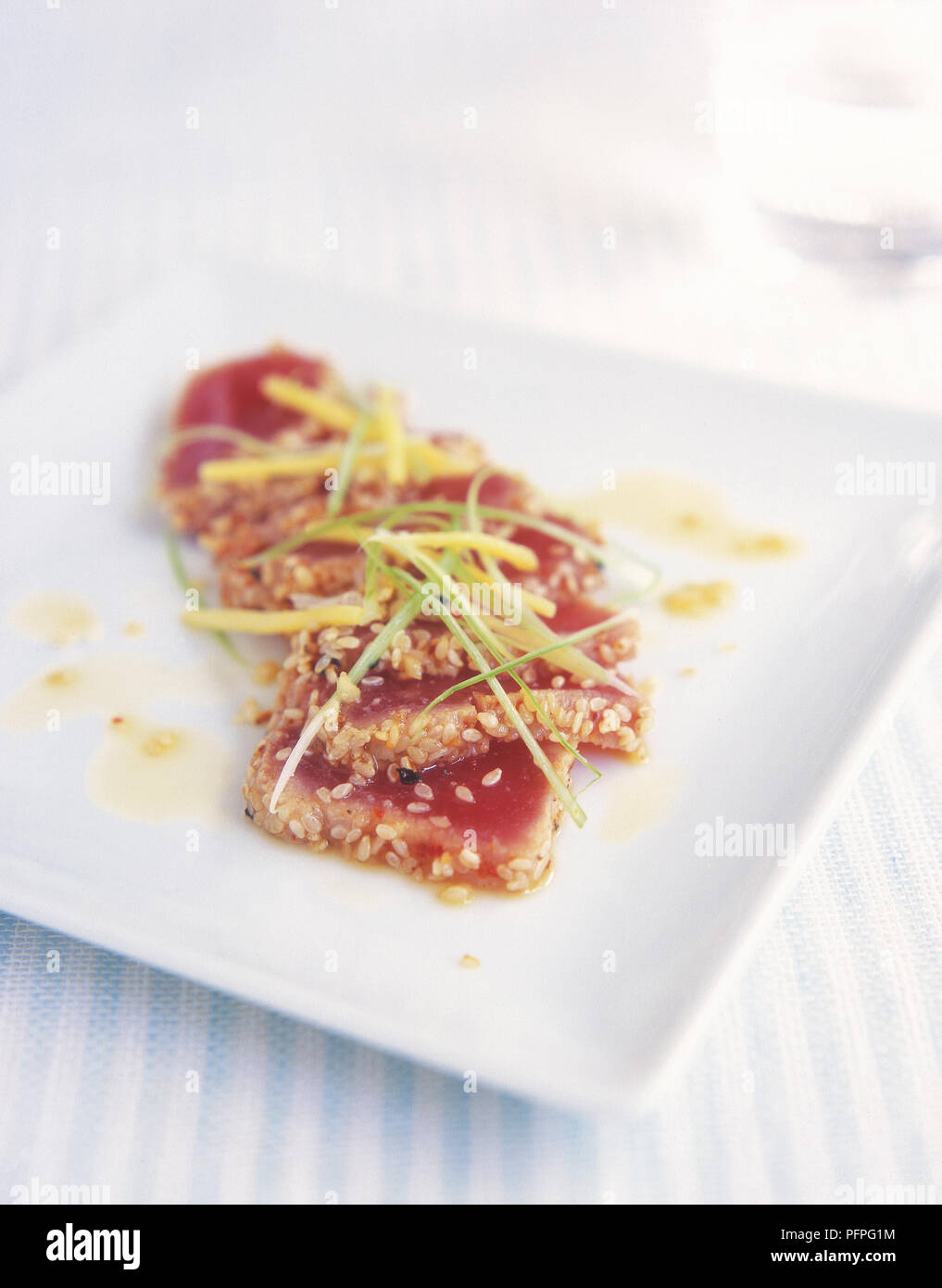 Chilled seared tuna with ginger and spring onion dressing (Katsuo tataki) sprinkled with sesame seeds on white plate, close-up Stock Photo