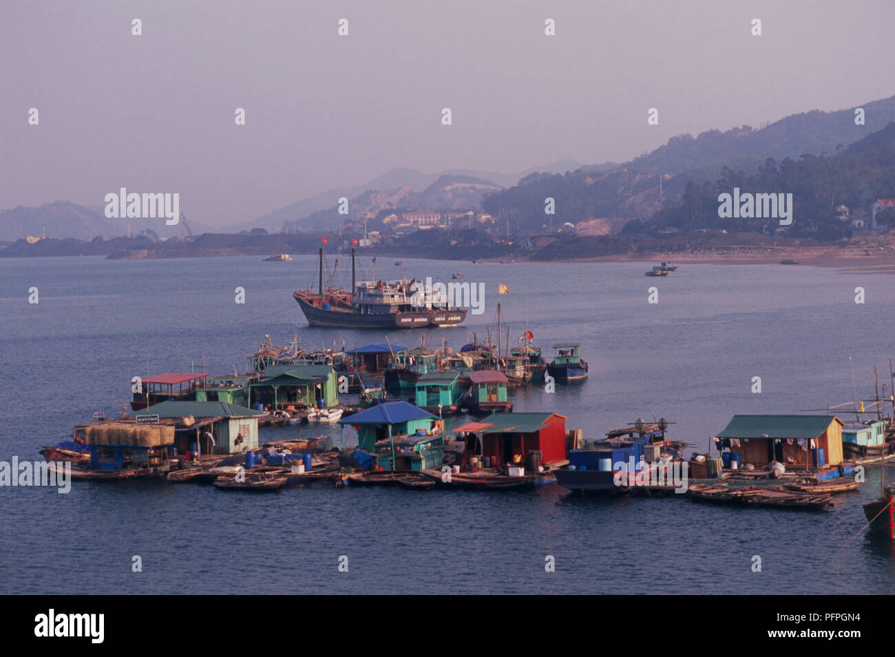 Vietnam, Bai Tu Long Bay, floating fishing village near coastline with ship in background Stock Photo