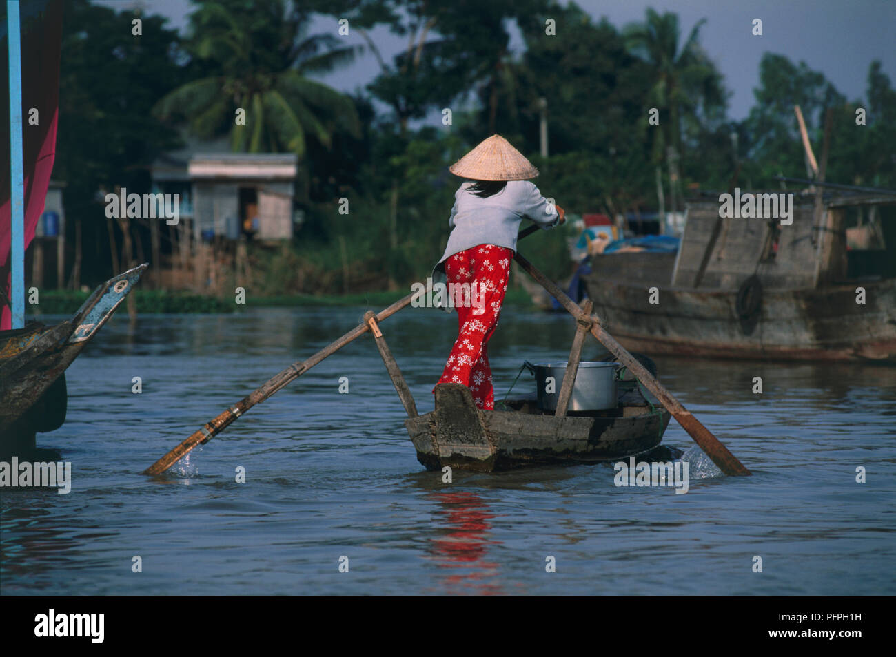 Vietnam, Mekong Delta, woman rowing sampan boat on river with long oars Stock Photo