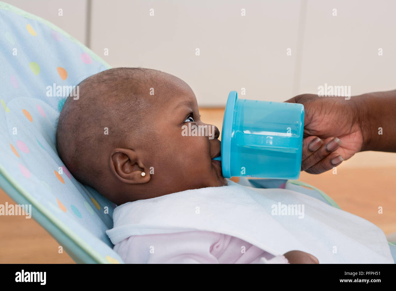Baby girl in soft seat being fed drink from plastic cup, close-up Stock Photo