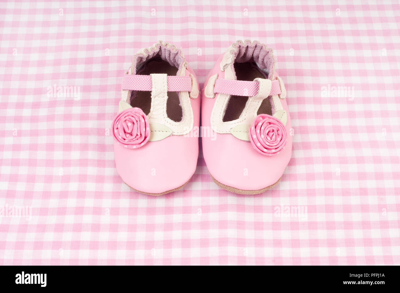Pair of soft pink and white baby's shoes decorated with pink roses on pink and white checked background Stock Photo