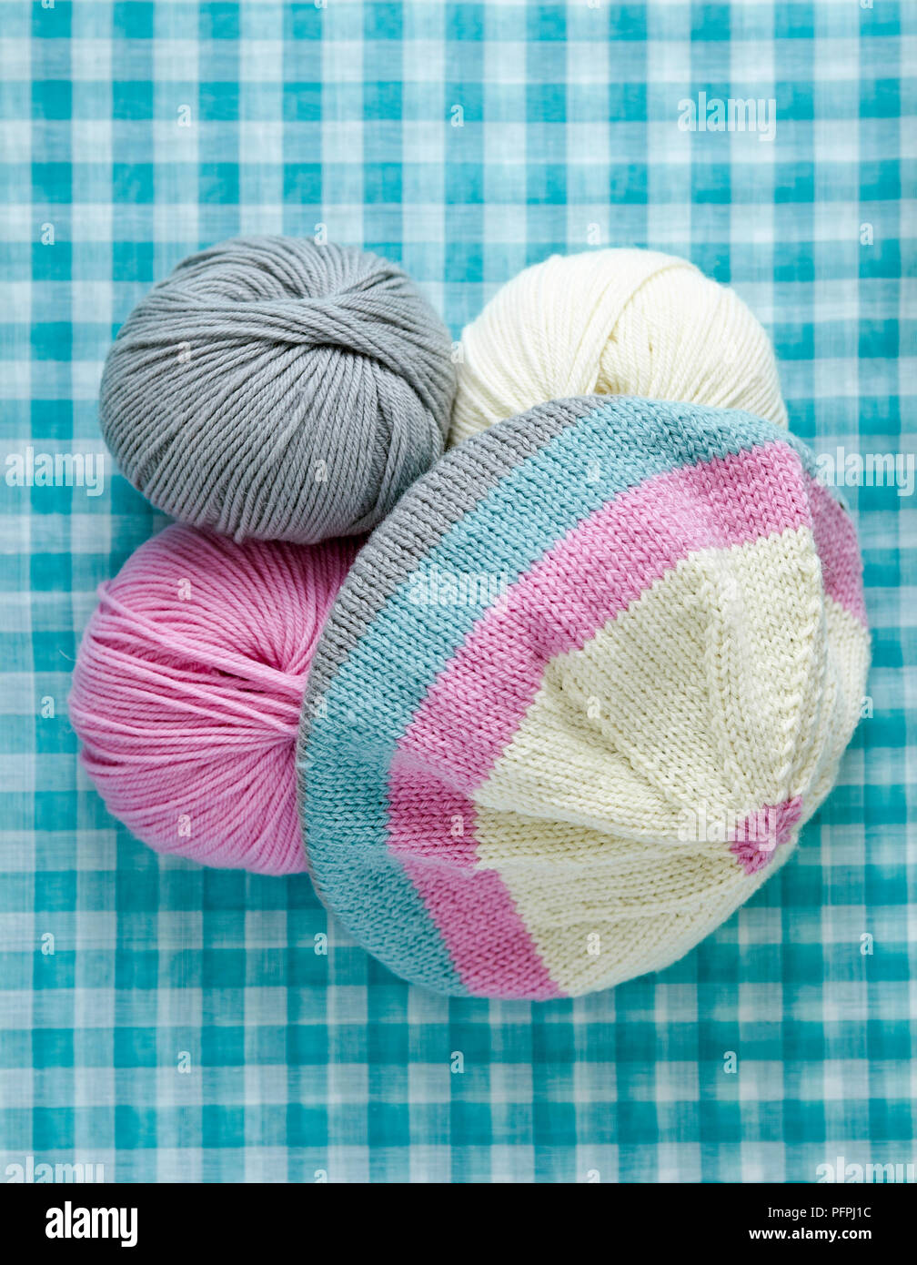 Stripy beanie hat and balls of wool on checked background Stock Photo