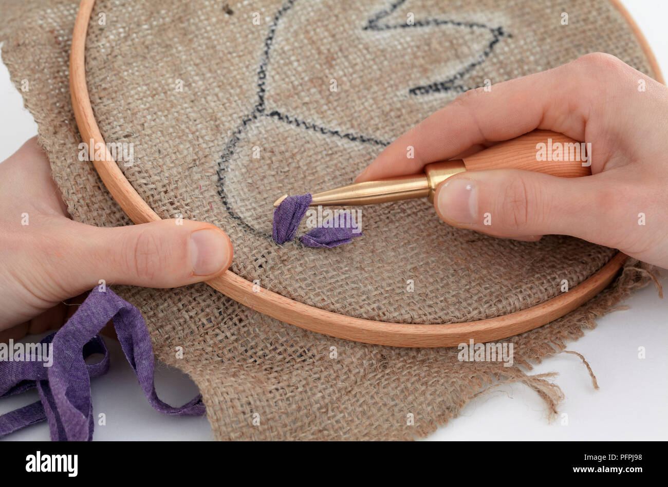 Pulling loop of fabric through hessian in embroidery hoop, using hook (making rag rugging design), close-up Stock Photo