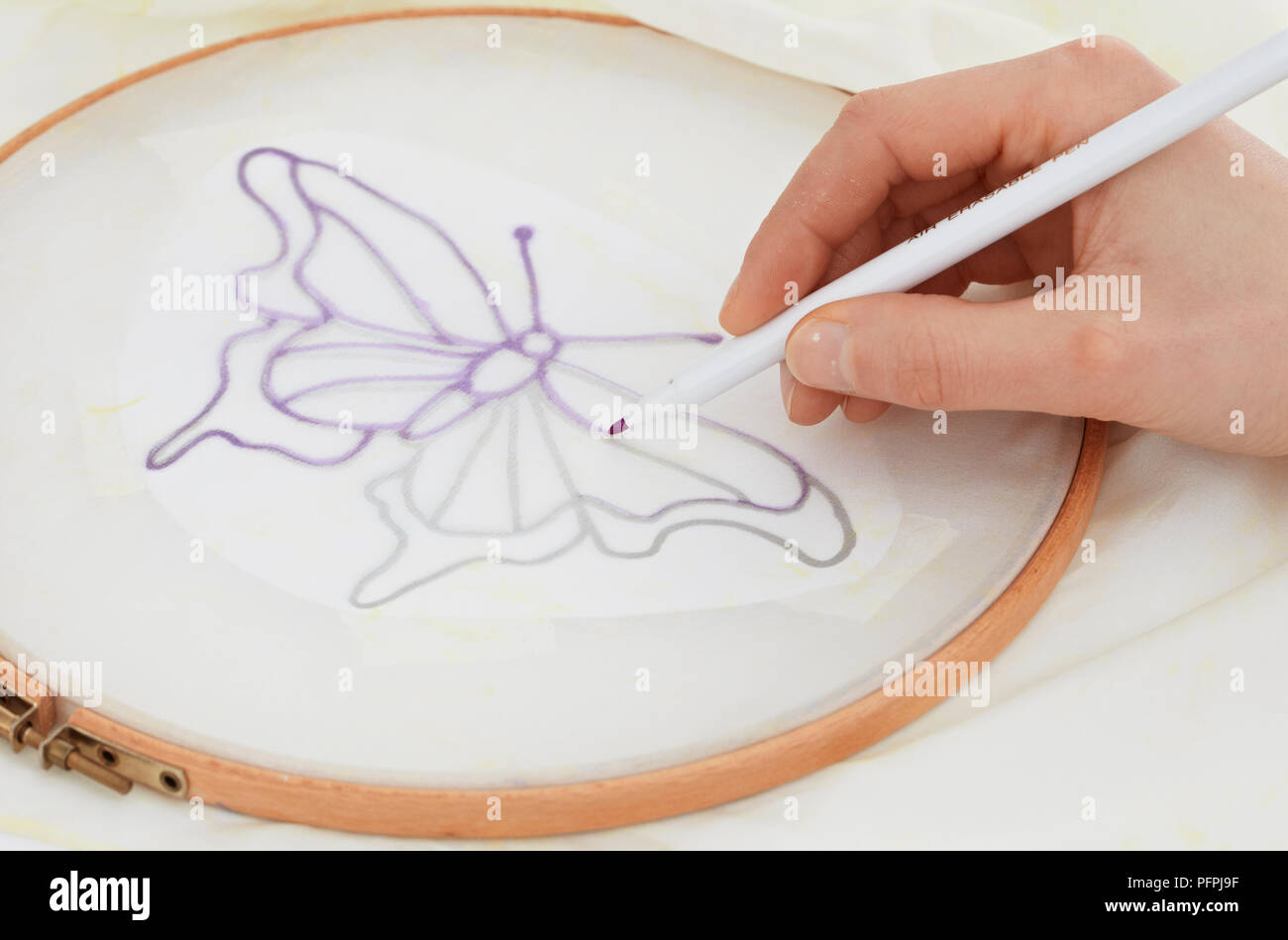 Tracing over lines of butterfly motif on silk scarf secured to embroidery hoop, close-up Stock Photo