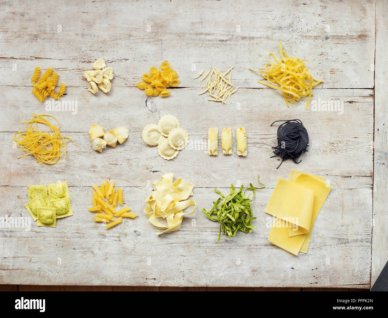 Different types of pasta on wood background, including filled pasta, ribbon pasta, pasta tubes, on wood background Stock Photo