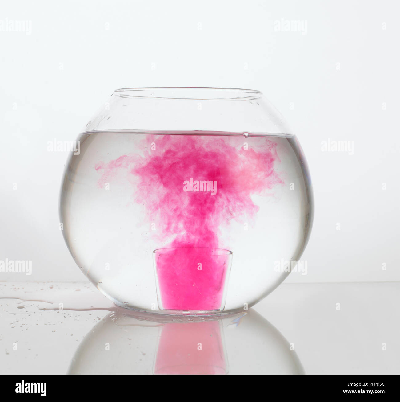 Pink dye dissolving in bowl of water Stock Photo