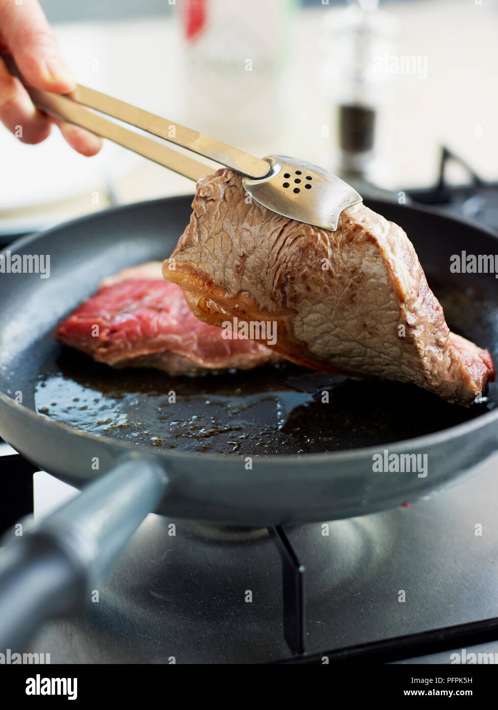 Lifting steak with tongs to check underside Stock Photo