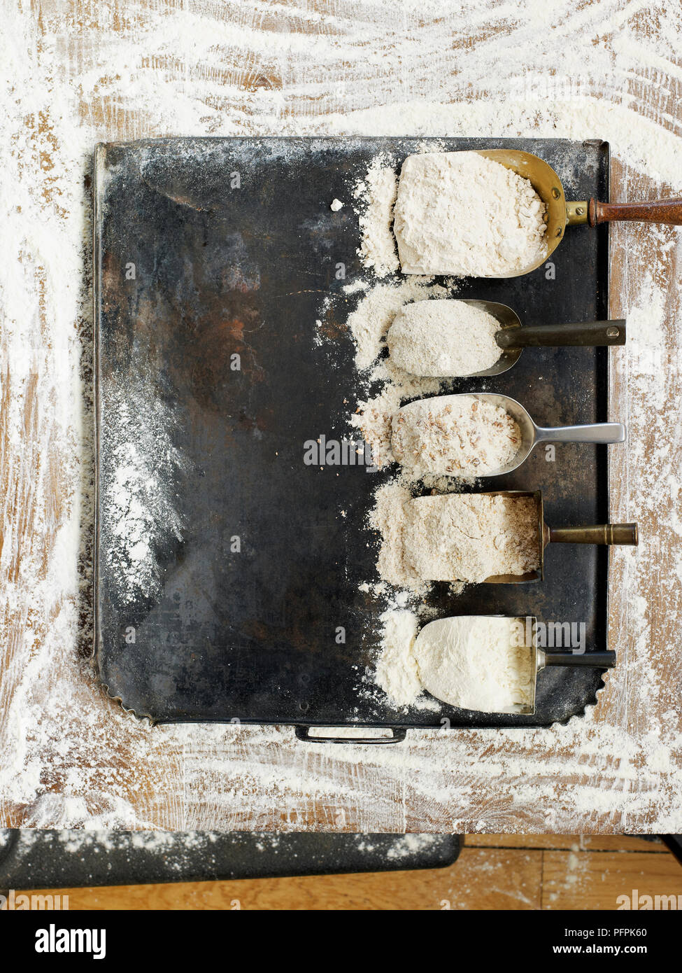 Row of scoops containing different types of flour, spelt, rye, granary, wholemeal, and white, on floured surface Stock Photo