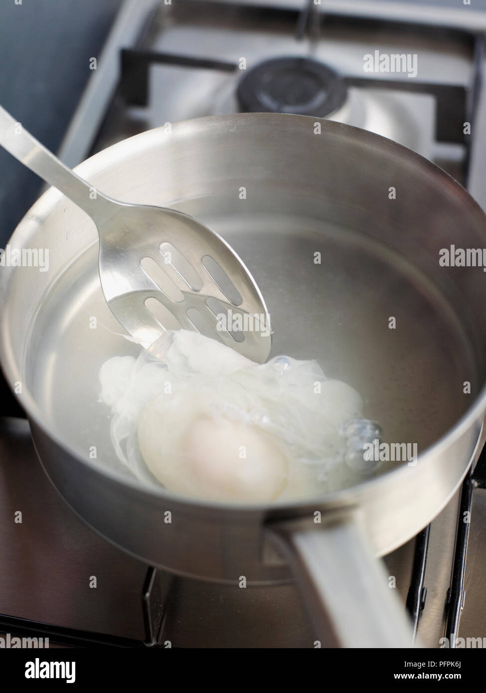 Lifting poached egg out of water with slotted spoon Stock Photo Alamy