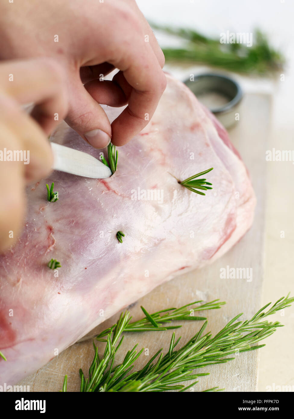 Studding leg of lamb with fresh rosemary, using tip of knife to insert sprigs in holes Stock Photo