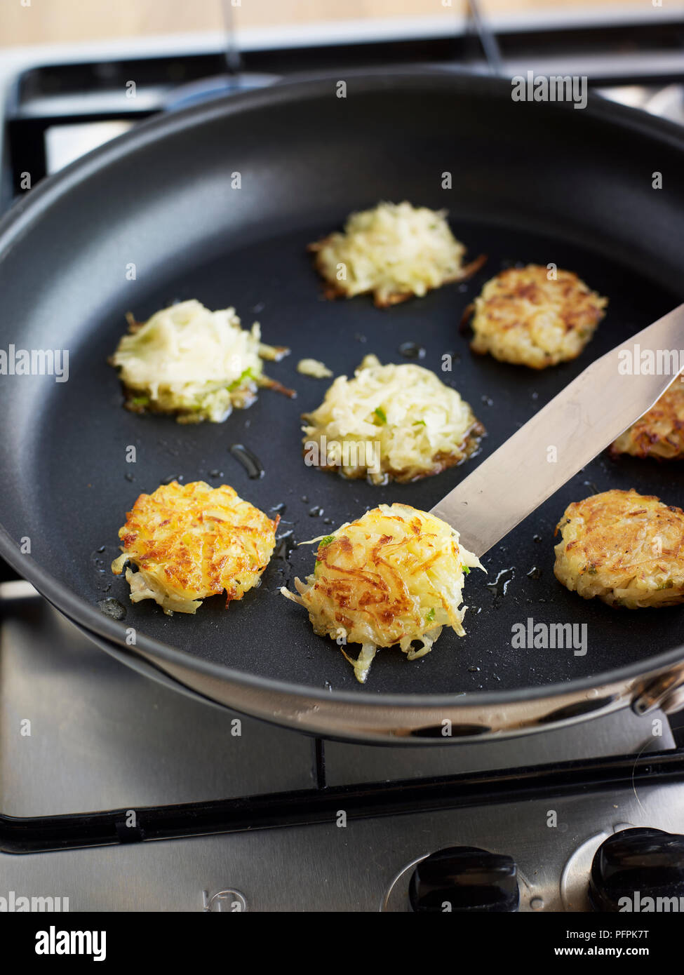 Frying crab-mangetout roesti (rosti) in frying pan using a palette knife to turn over Stock Photo
