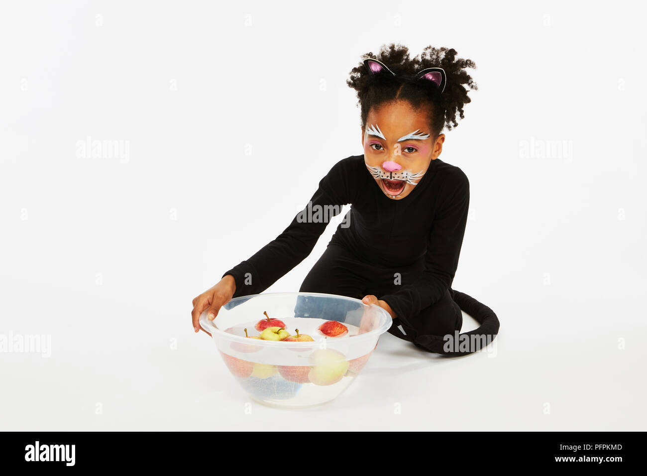Girl dressed as a black cat with a bowl of apples Stock Photo