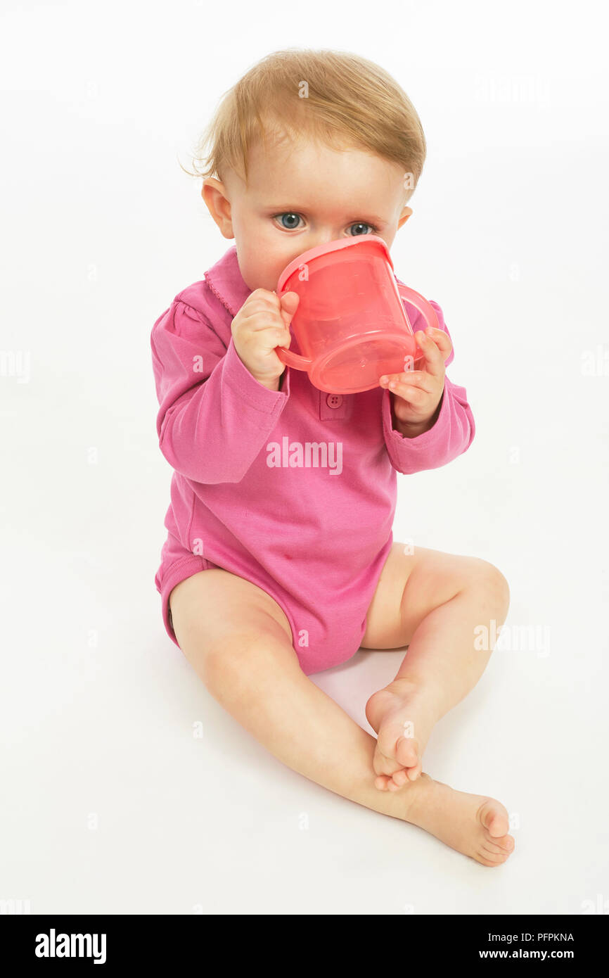 Baby in pink playsuit drinking  (Model age - 9 months) Stock Photo