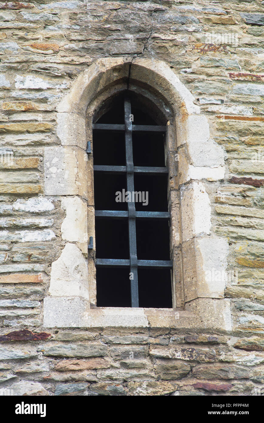 Tall narrow barred window in stone wall. Stock Photo