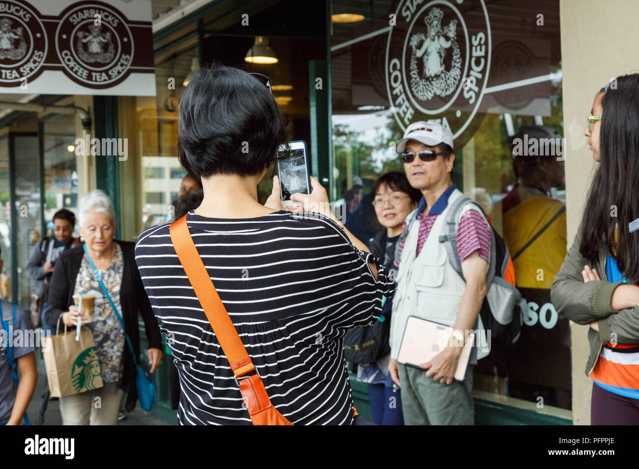 Visitors Take Pictures In Front Of Original Logo Printed Window Starbucks Coffee Flagship Store At Pike Place Market Seattle USA Visitors Take Pictures In Front Of Original Logo Printed Window Starbucks Coffee Flagship Store At Pike Place Market Seattle USA