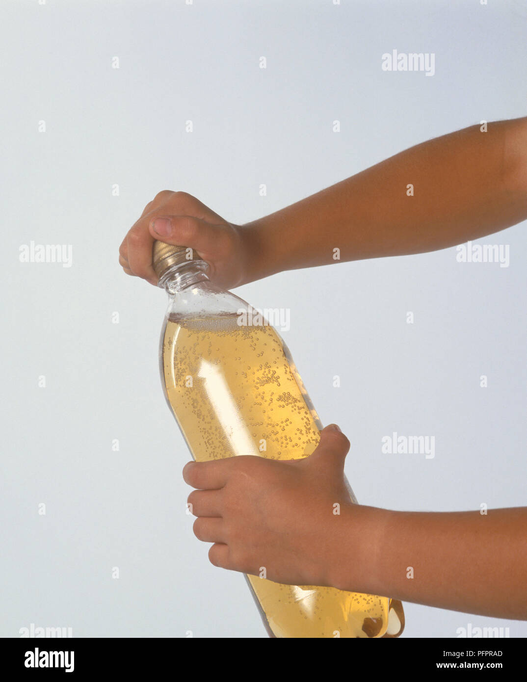 Child unscrewing the top from a plastic bottle containing fizzy soft