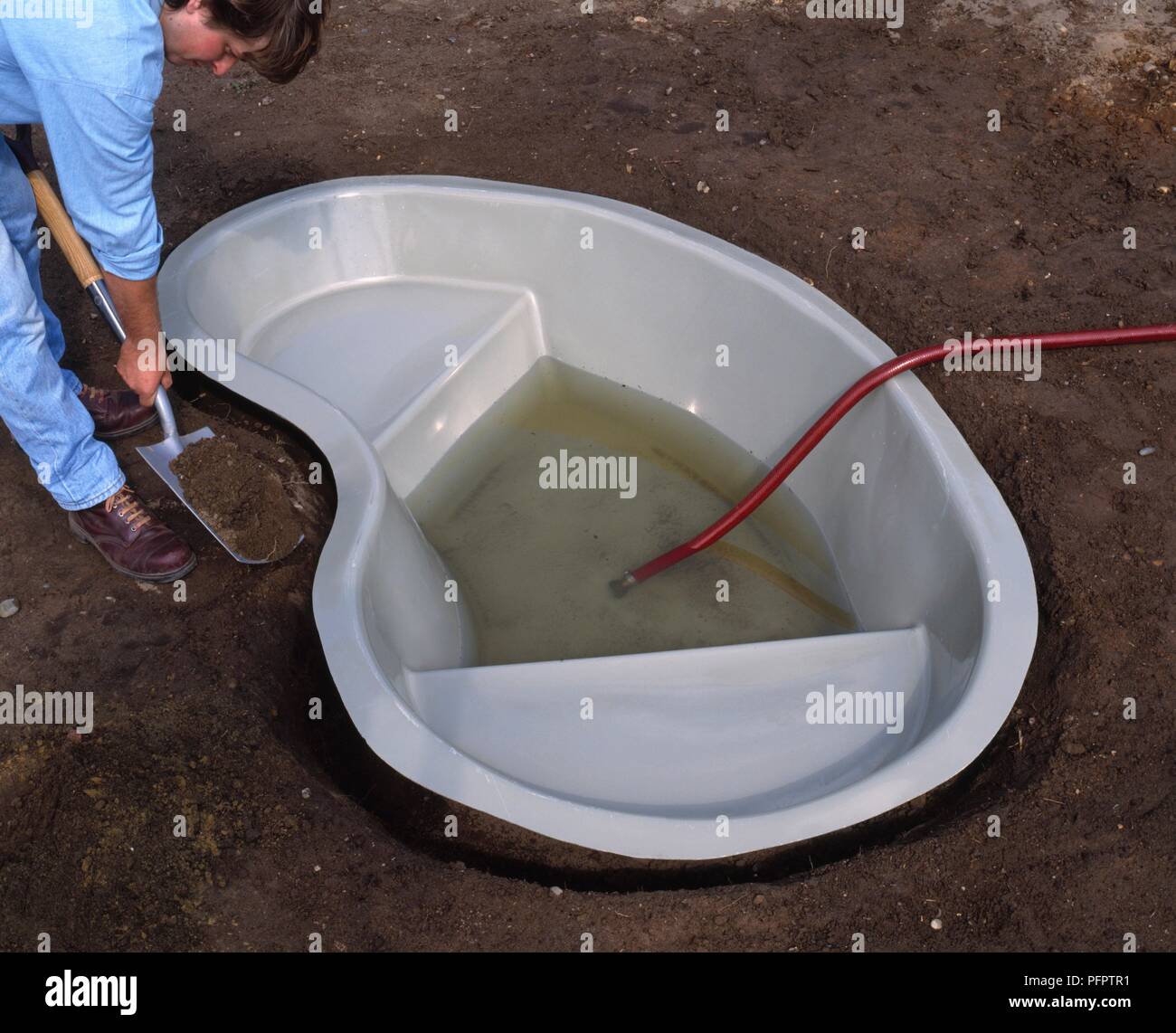 Pond mould being filled up with water through a hose pipe Stock Photo