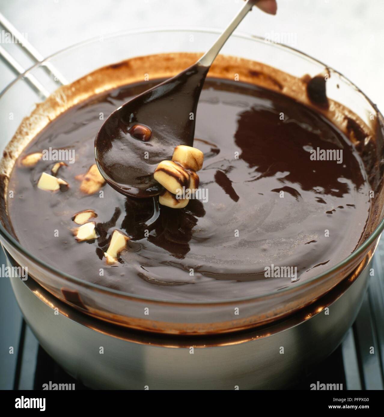 Using spoon to add nuts to melted chocolate in glass bowl above saucepan on hob Stock Photo Alamy