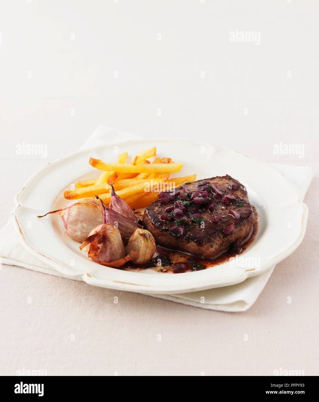 Minute steak with roasted garlic, red onions and French fries, on a plate Stock Photo