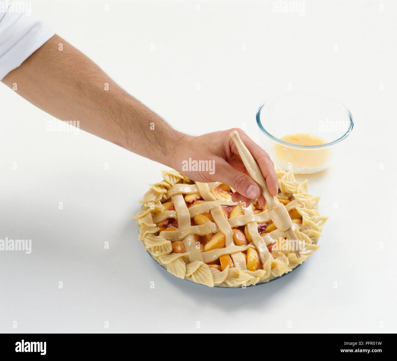 Using basting brush to apply egg yolk on top of fruit pie Stock Photo