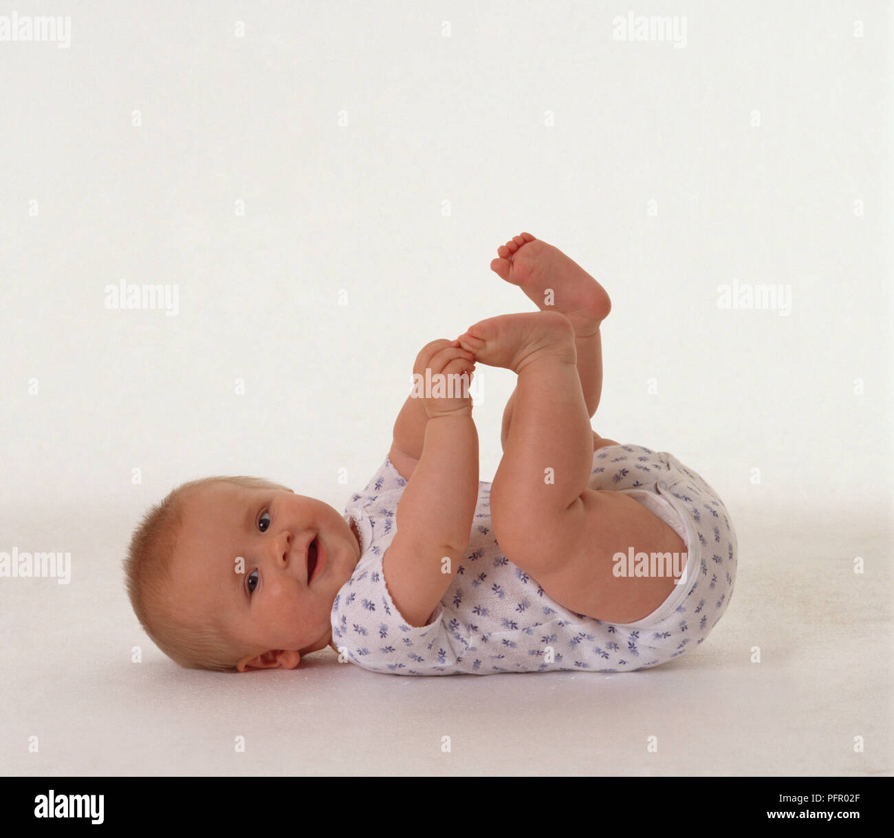 Smiling baby girl lying on back with legs and arms up Stock Photo
