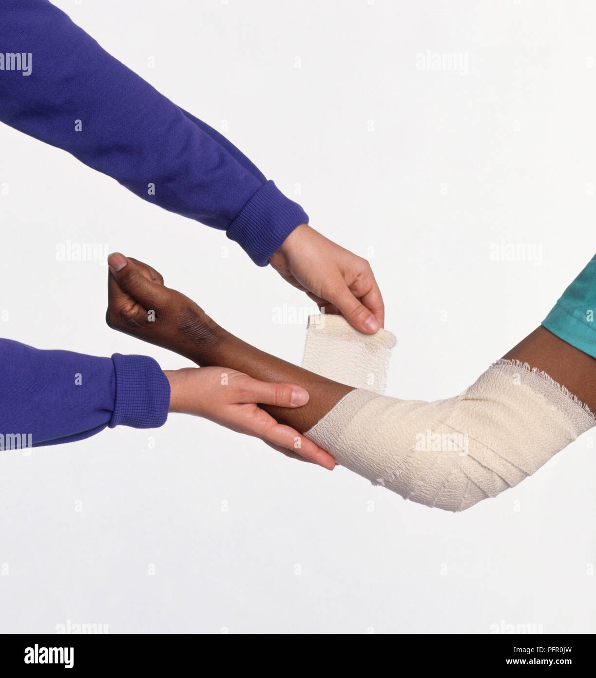 Woman wrapping bandage around arm and elbow of injured person Stock