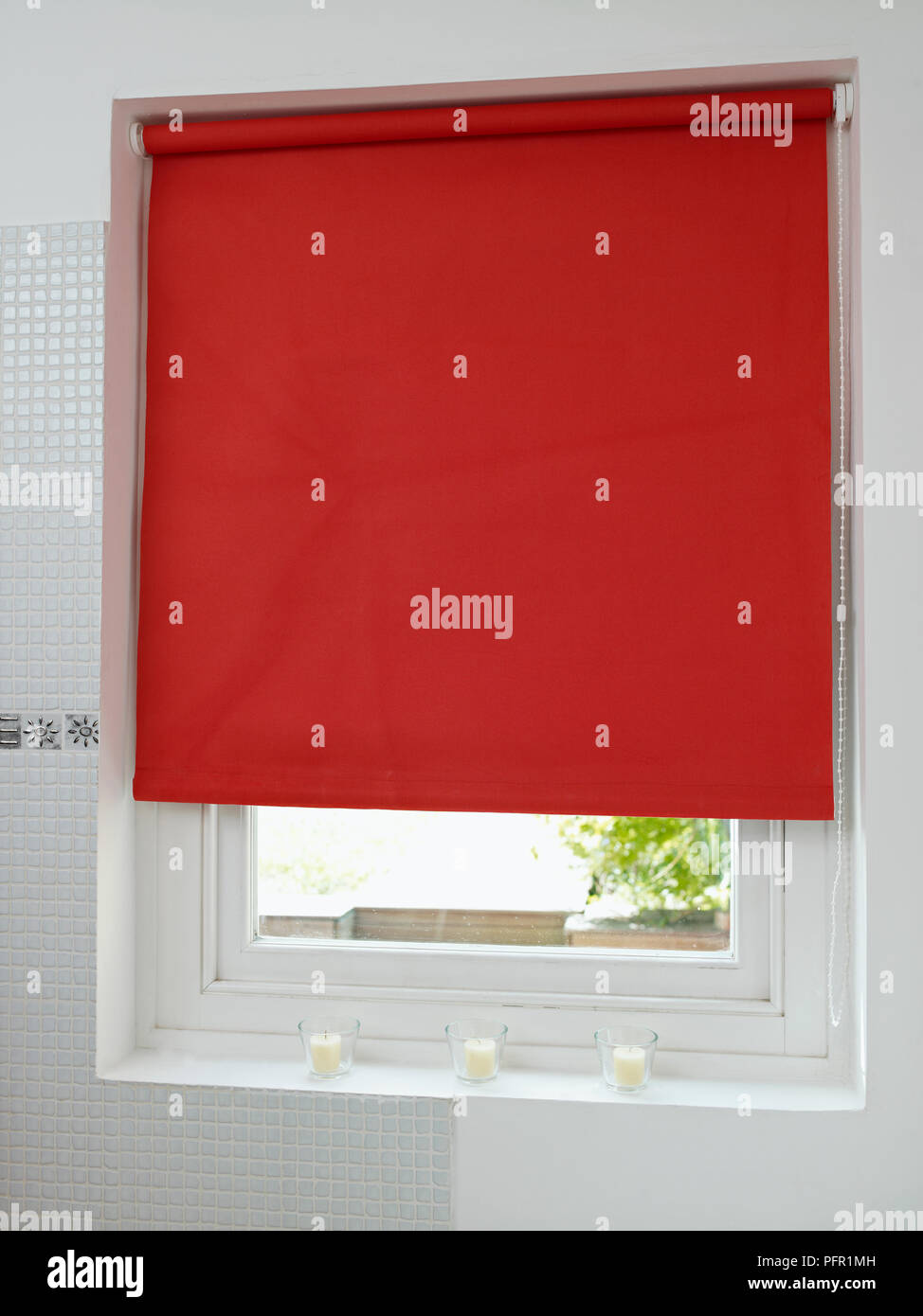 Red roller blind three quarters closed over bathroom window, close-up Stock Photo
