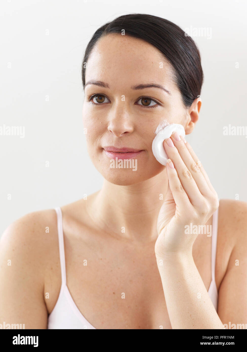 Woman applying cleansing lotion to face, using cotton wool pad Stock