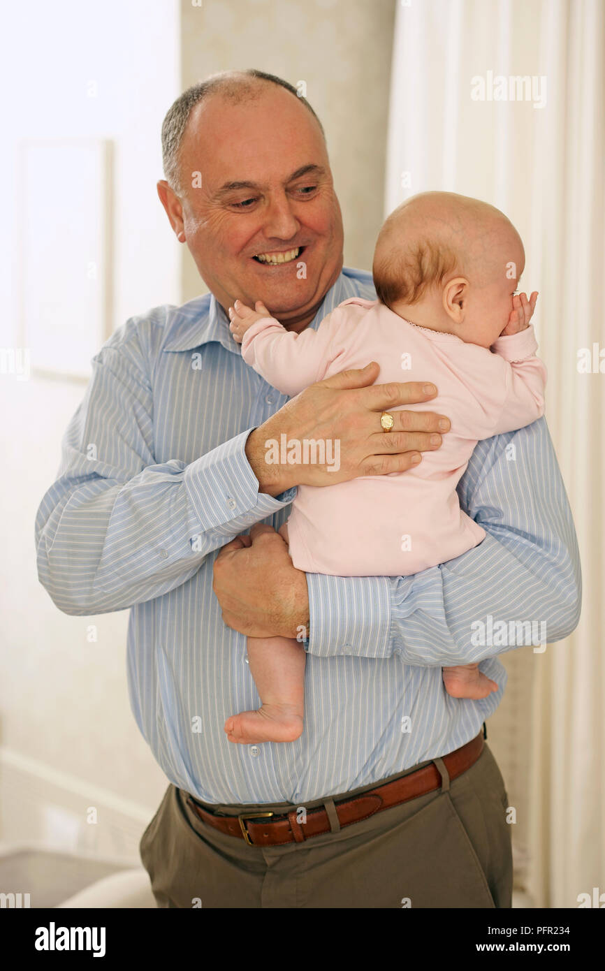 Grandfather standing holding baby granddaughter in his arms, smiling ...