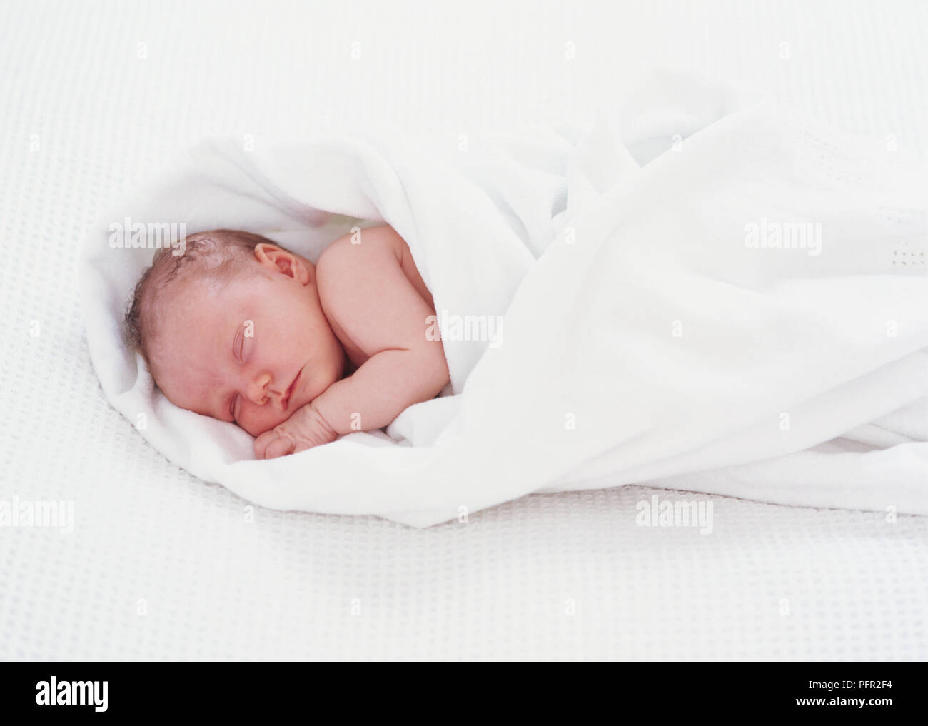 Newborn baby girl sleeping, wrapped in white blanket Stock Photo