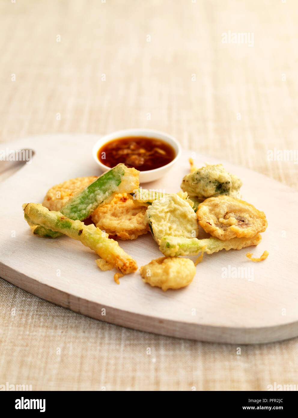 Deep fried vegetable tempura on wooden chopping board with bowl of