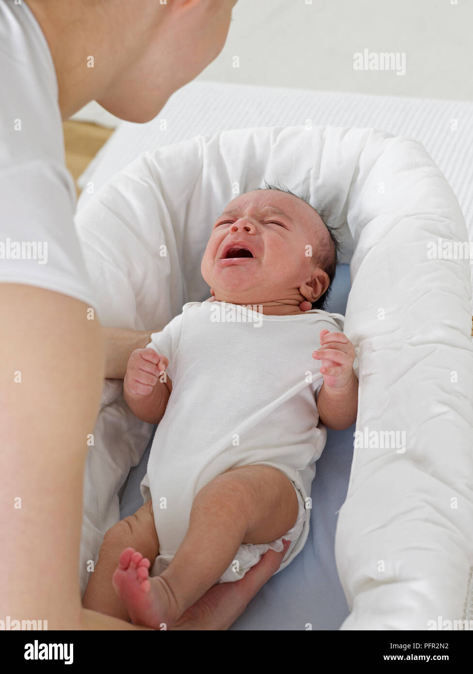 Woman picking up crying baby boy from crib, 9 weeks Stock Photo Alamy