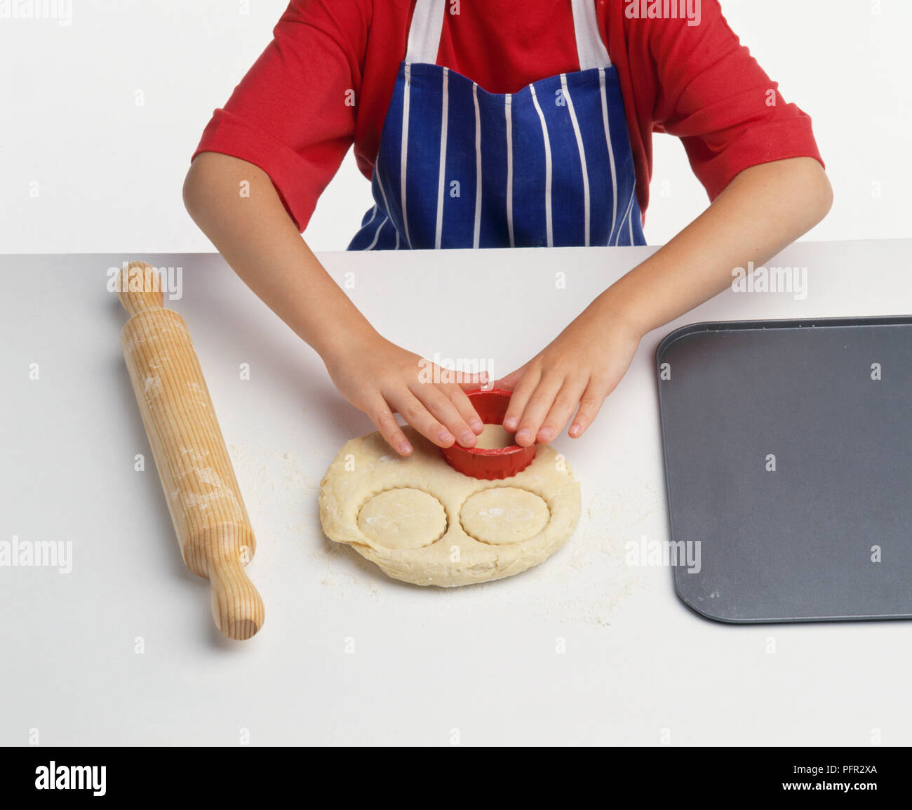 Child making scones, using cutter on a piece of rolled-out dough Stock Photo