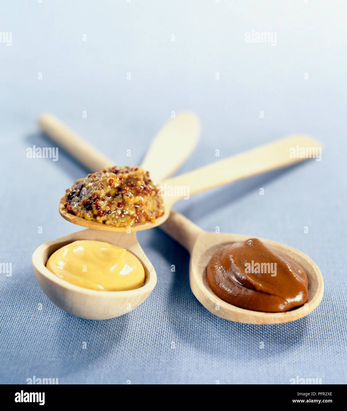 Different types of mustard on wooden spoons, including wholegrain