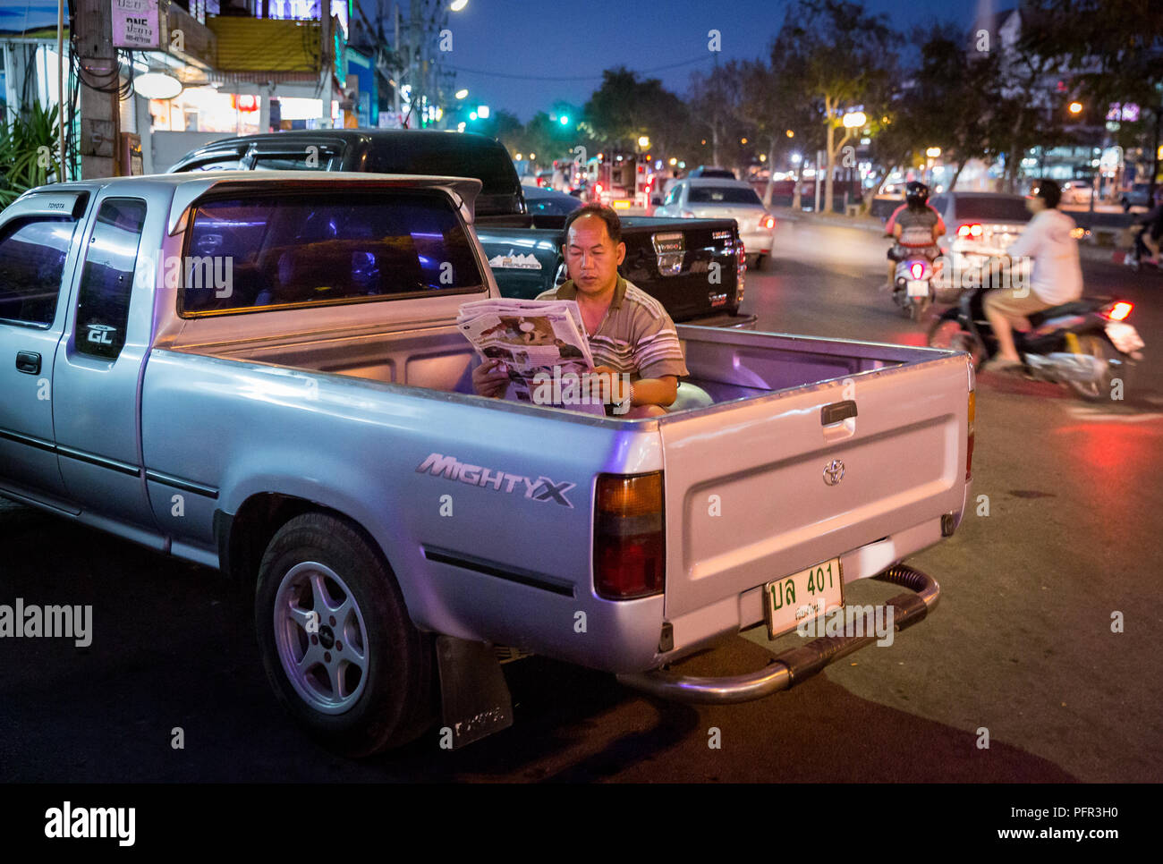 Man sitting in the back of a pickup truck, reading a newspaper, in Chiang Mai, Thailand Stock